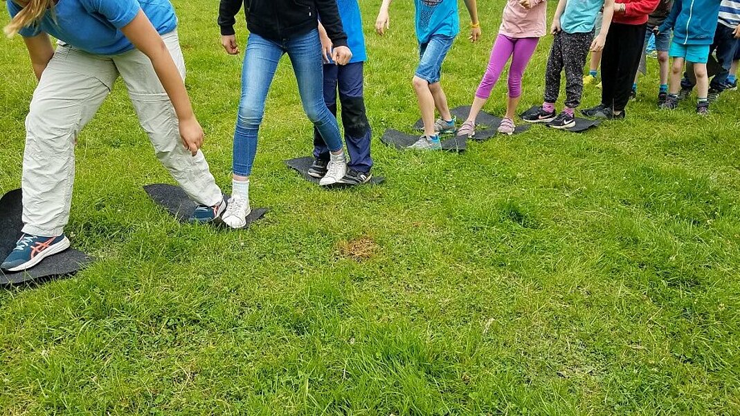 Kinder hintereinander in einer Reihe auf grüner Wiese.