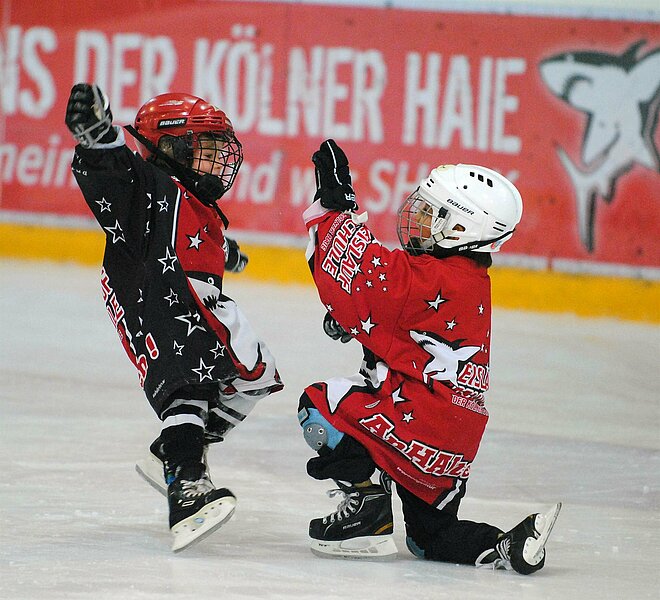 Zwei Kinder jubeln in Eishockeymontur auf dem Eis.