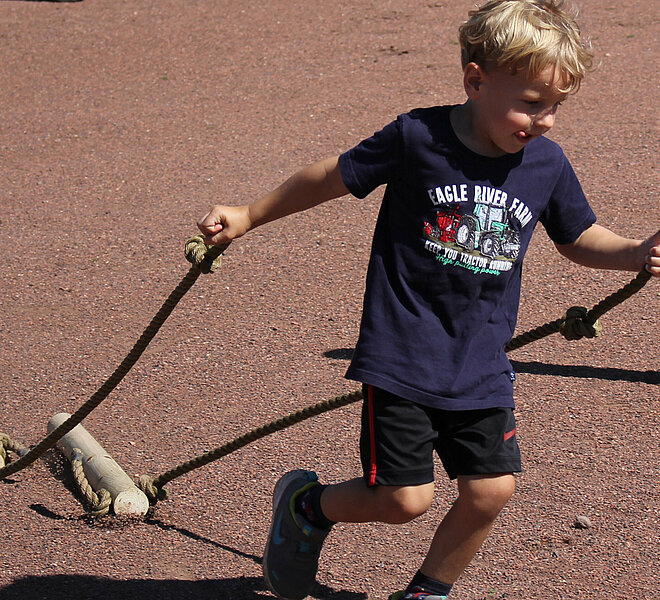 Kind läuft mit Gewichten an Seilen über Ascheplatz.
