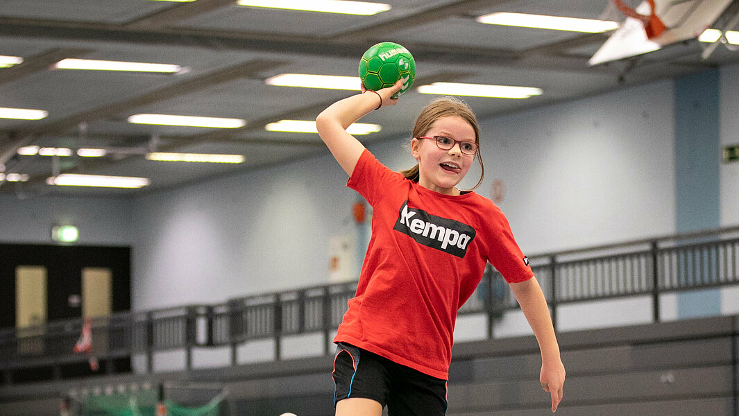 Mädchen in Wurfbewegung mit einem grünen Handballl in der Hand.
