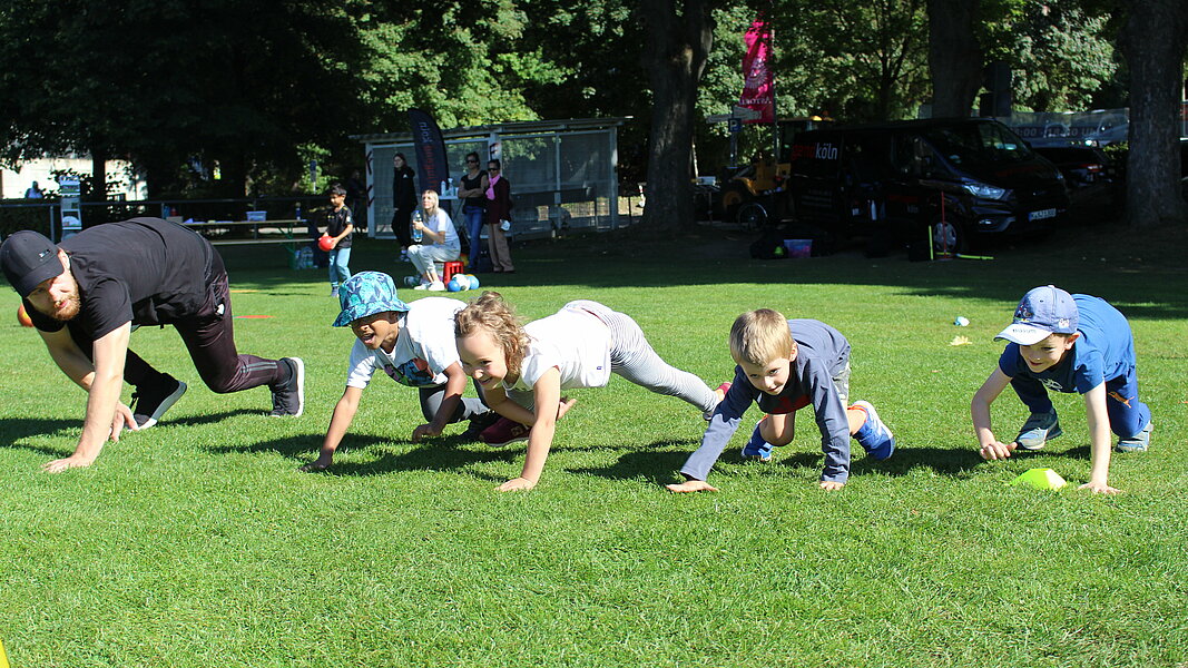 Kinder machen Sportübungen auf einer Wiese und haben dabei viel Spaß.