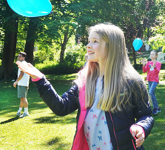 Mädchen wirft blauen Luftballon in die Luft.