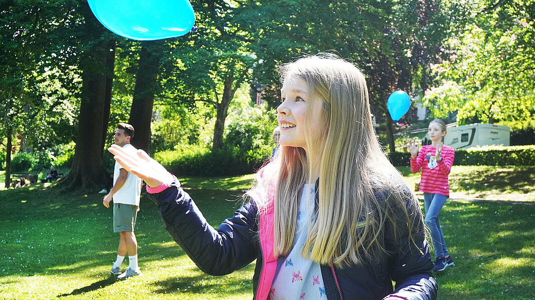 Mädchen wirft blauen Luftballon in die Luft.
