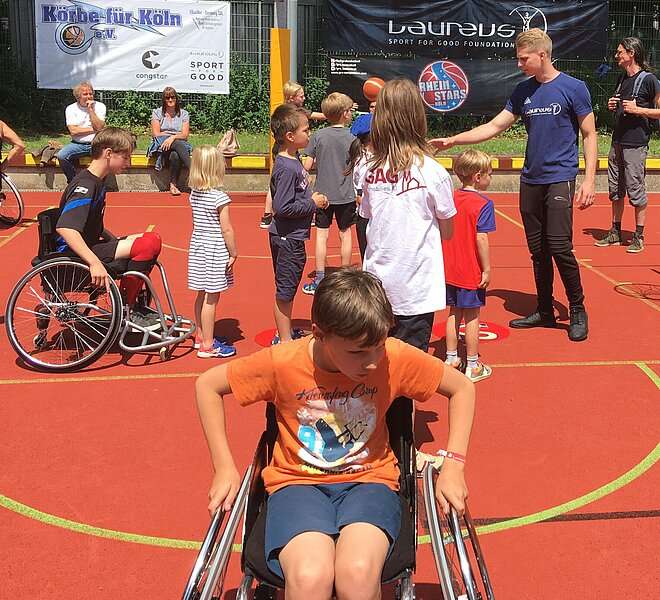 Kinder mit und ohne Rollstuhl spielen Basketball auf einem Platz.