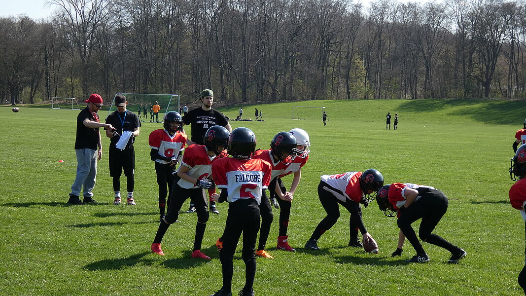 Kinder beim American Football Training auf einer Wiese.