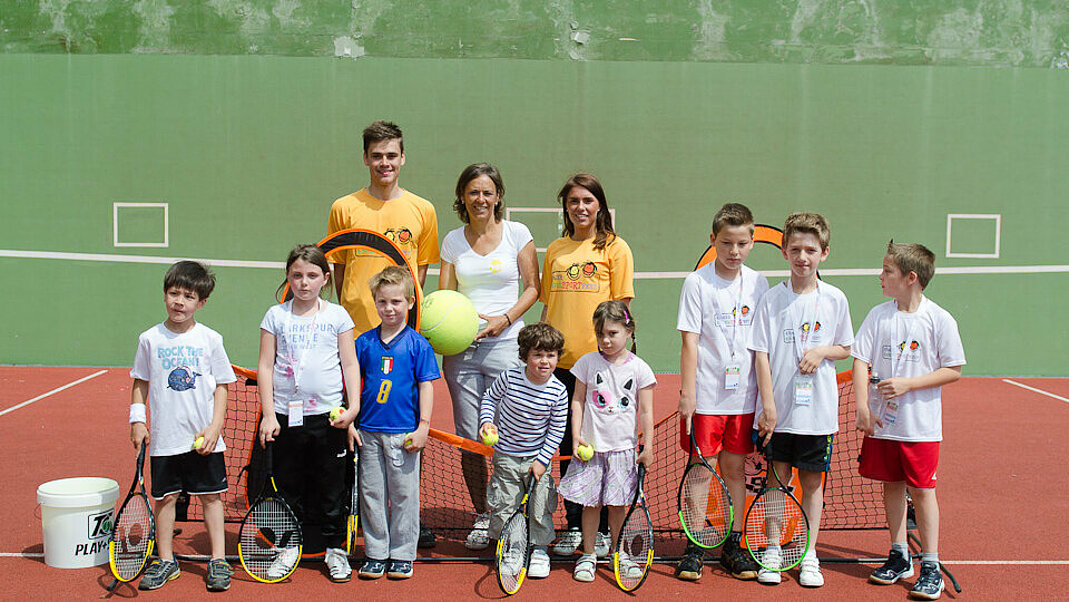 Kinder und Trainer:innen stehen gemeinsam auf einem Tennisplatz.