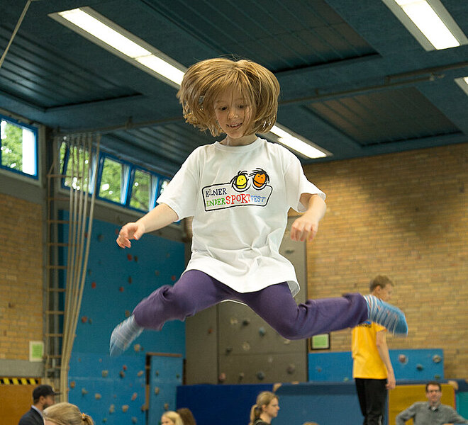 Kind springt auf einem Trampolin in einer Halle.